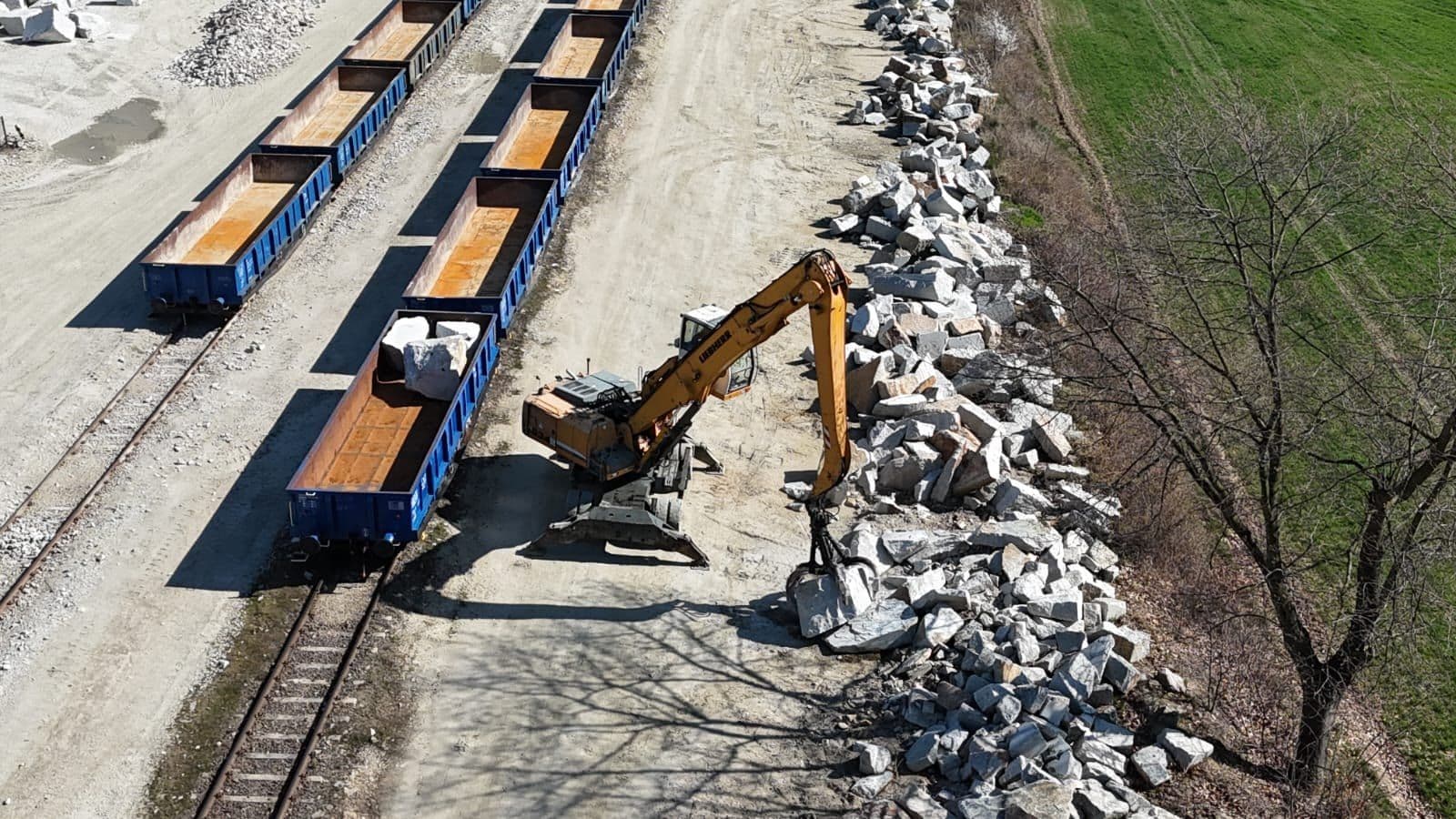 Widok z drona na skład wagonów z kamieniem hydrotechnicznym i koparkę przeładunkową przy torach